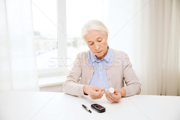 senior woman with glucometer checking blood sugar Stock photo © dolgachov