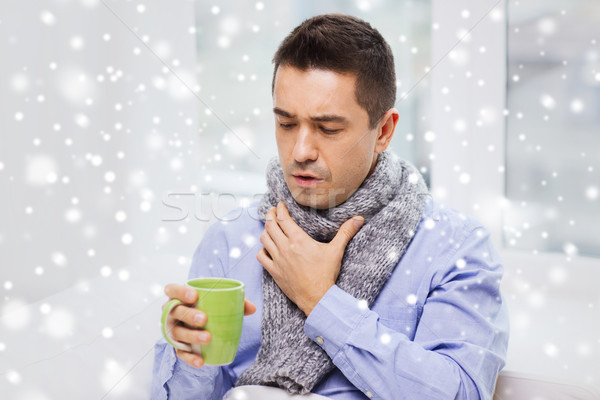 Stock photo: ill man with flu drinking tea and coughing at home