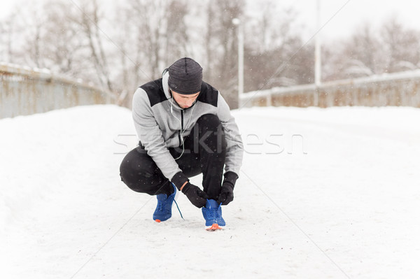 man with earphones tying sports shoe in winter Stock photo © dolgachov