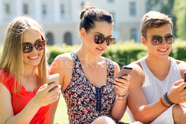 Stock photo: smiling friends with smartphones sitting on grass