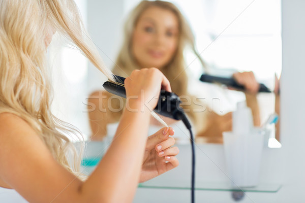 woman with styling iron straightening hair at home Stock photo © dolgachov