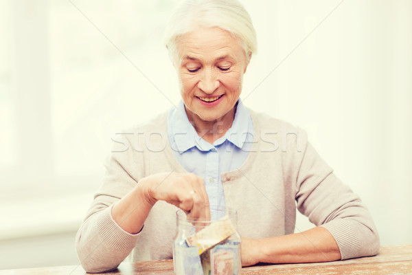 senior woman putting money into glass jar at home Stock photo © dolgachov