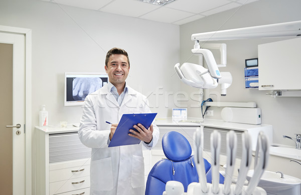 happy male dentist with clipboard at dental clinic Stock photo © dolgachov