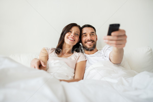 Stock photo: happy couple lying in bed at home and watching tv