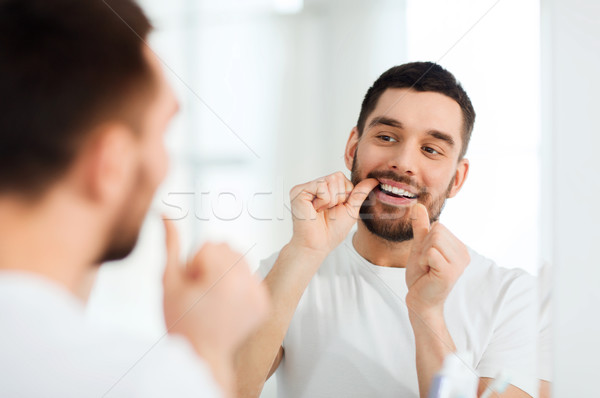man with dental floss cleaning teeth at bathroom Stock photo © dolgachov