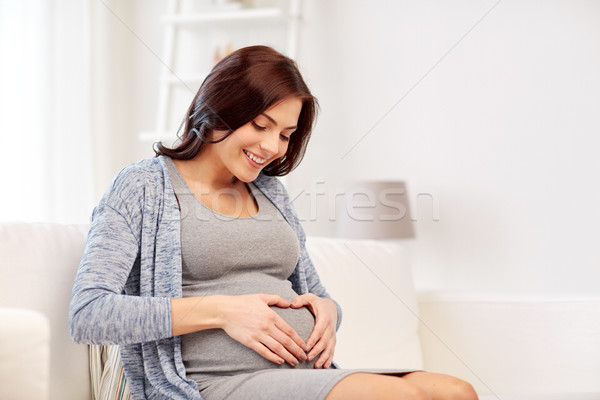 Stock photo: happy pregnant woman making heart gesture at home