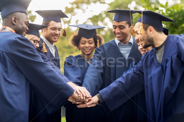 happy students in mortar boards with hands on top Stock photo © dolgachov