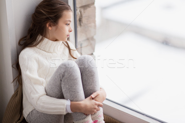 sad girl sitting on sill at home window in winter Stock photo © dolgachov