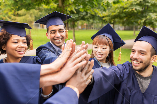 happy students in mortar boards making high five Stock photo © dolgachov