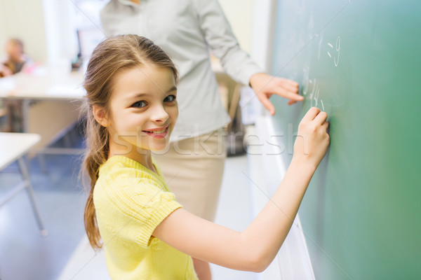 Stock photo: little smiling schoolgirl writing on chalk board