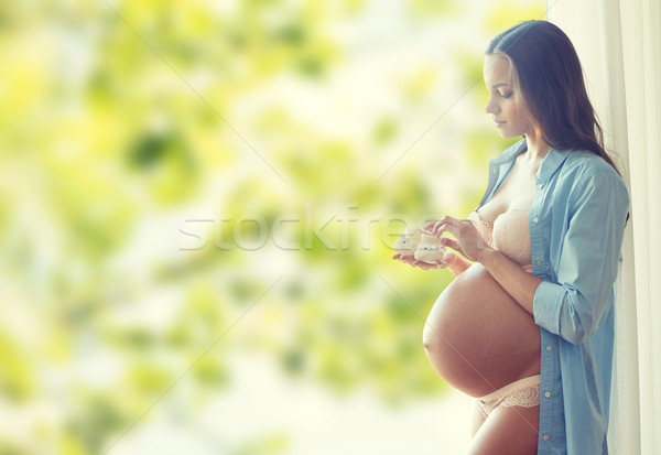 Stock photo: happy pregnant woman with baby booties at home