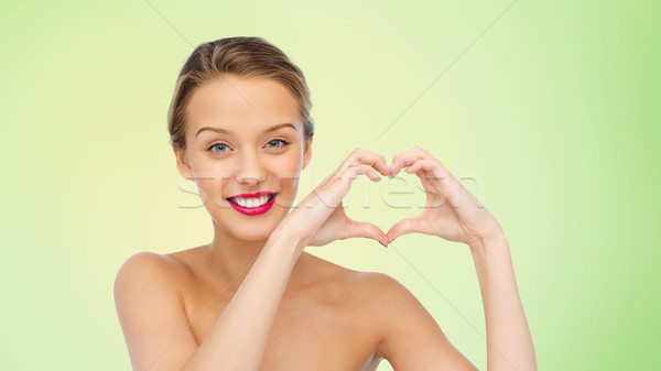 Stock photo: smiling young woman showing heart shape hand sign