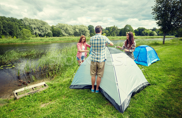 group of smiling friends setting up tent outdoors Stock photo © dolgachov