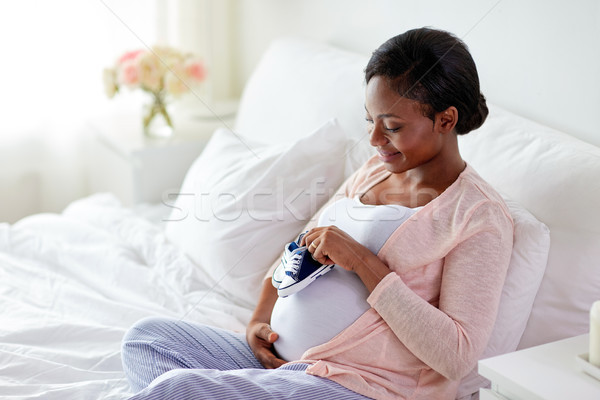 Stock photo: pregnant african woman with baby bootees in bed