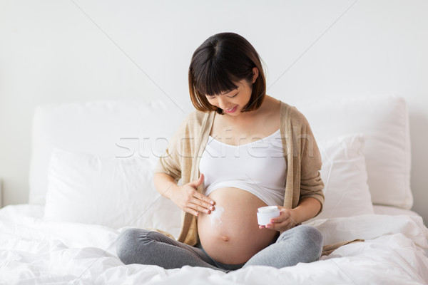 happy asian pregnant woman applying cream to belly Stock photo © dolgachov