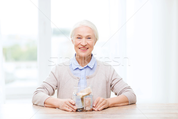 senior woman with money in glass jar at home Stock photo © dolgachov