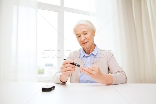 senior woman with glucometer checking blood sugar Stock photo © dolgachov