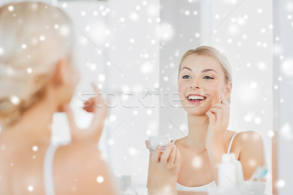 happy woman applying cream to face at bathroom Stock photo © dolgachov