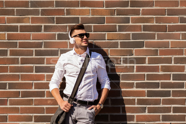 young man in headphones with bag over brickwall Stock photo © dolgachov