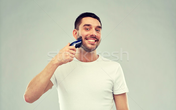 smiling man shaving beard with trimmer over gray Stock photo © dolgachov