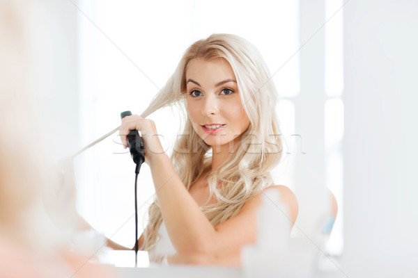 woman with styling iron doing her hair at bathroom Stock photo © dolgachov