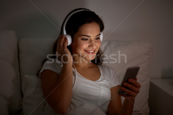 Stock photo: woman with smartphone and headphones in bed