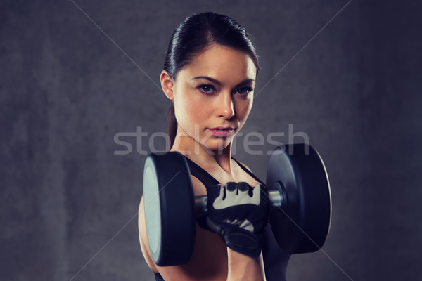 Stock photo: young woman flexing muscles with dumbbells in gym