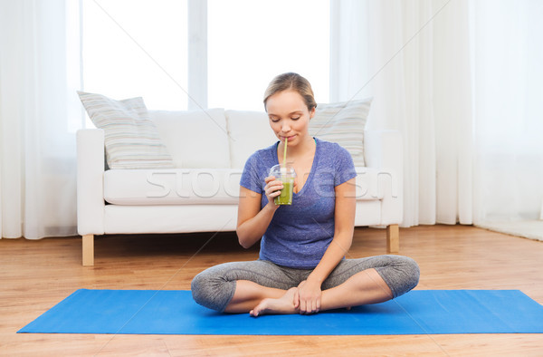 happy woman with smoothie sitting on mat at home Stock photo © dolgachov
