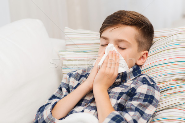 ill boy lying in bed and blowing his nose at home Stock photo © dolgachov