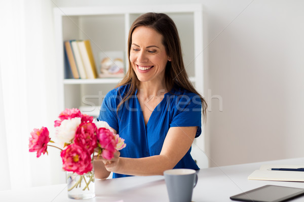 Stock photo: woman setting flowers in vase on office table