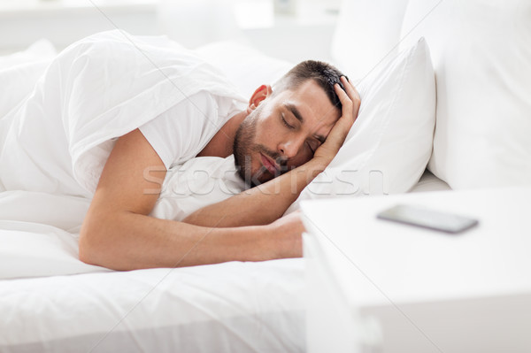 man sleeping in bed with smartphone on nightstand Stock photo © dolgachov