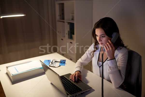Stock photo: woman with laptop calling on phone at night office
