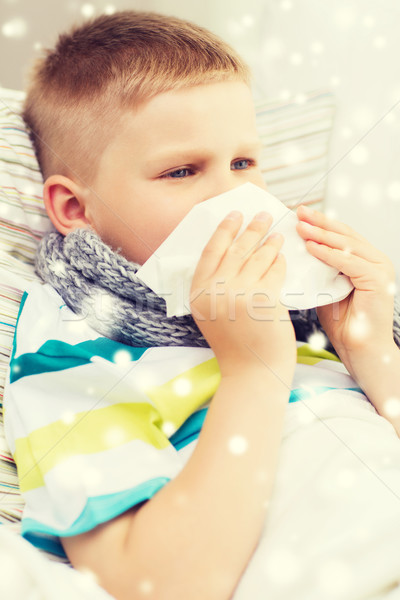 ill boy blowing nose with tissue at home Stock photo © dolgachov