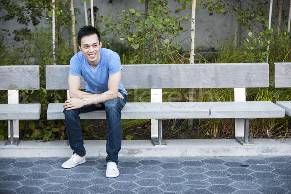 Happy young asian man on bench Stock photo © elenaphoto