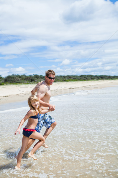 Happy father and daughter running along beach in shallow water Stock photo © ElinaManninen