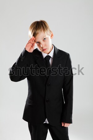 Serious young boy in black suit saluting Stock photo © ElinaManninen