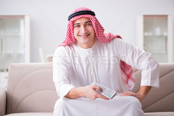 Stock photo: Young arab man watching tv sitting on the sofa