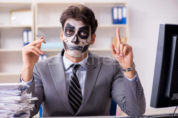 Businessmsn with scary face mask working in office Stock photo © Elnur