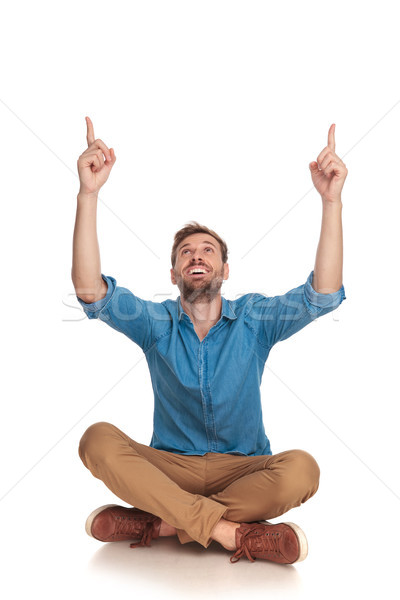 young smiling casual man is sitting and pointing up Stock photo © feedough