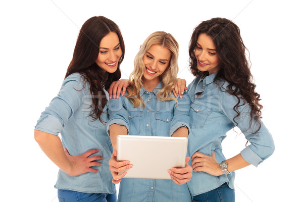 three smiling women looking at the screen of a tablet Stock photo © feedough