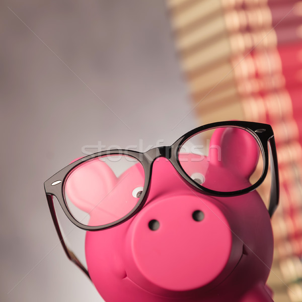 Stock photo: closeup of a piggy bank wearing glasses near books