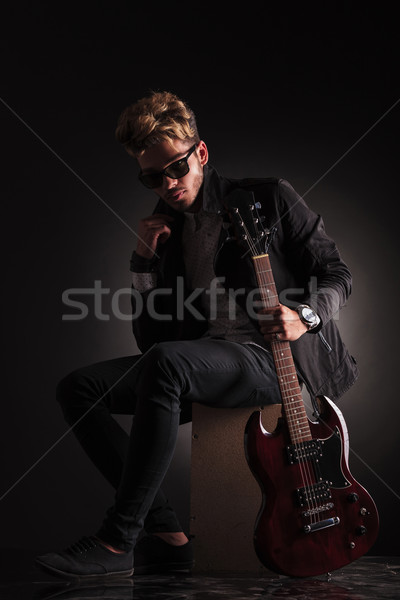 Stock photo: young guitarist sitting and holding his jacket by it's collar