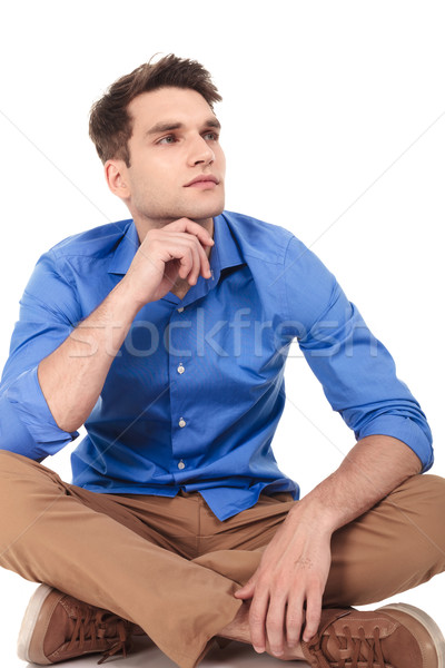 Pensive jeune homme séance jambes croisées caméra [[stock_photo]] © feedough