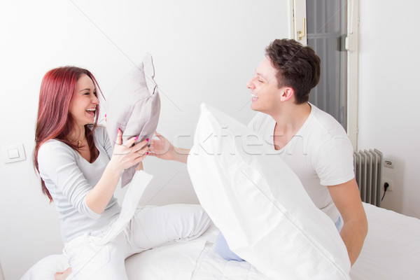 smiling man and woman fighting with pillows together in bed Stock photo © feelphotoart