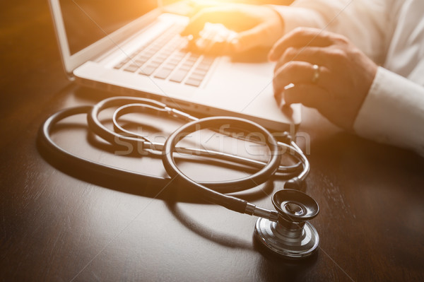 Medical Stethoscope Resting on Desk As Male Hands Type on Comput Stock photo © feverpitch