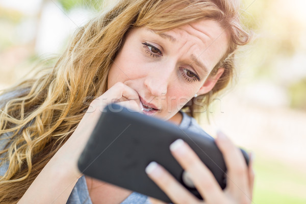Concerned Young Woman Outdoors Looking At Her Smart Phone. Stock photo © feverpitch