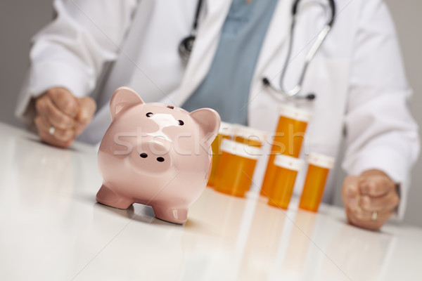 Doctor with Fists on Table Behind Bottle and Piggy Bank Stock photo © feverpitch