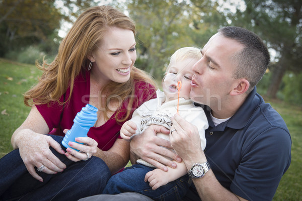 Stock photo: Young Parents Blowing Bubbles with their Child Boy in Park