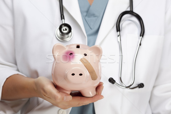 Doctor Holding Piggy Bank with Bruised Eye and Bandage Stock photo © feverpitch