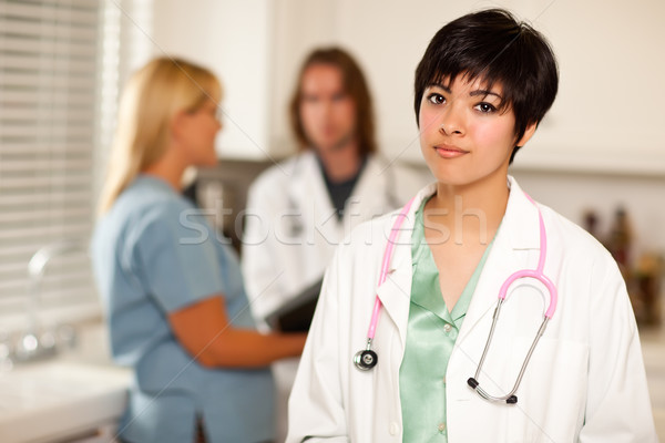 Stock photo: Pretty Latino Doctor Smiles at Camera as Colleagues Talk
